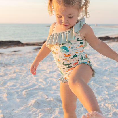 Young girl playing on the shore in her Florida-themed ruffle swimsuit, showcasing the stretchy, quick-dry fabric.