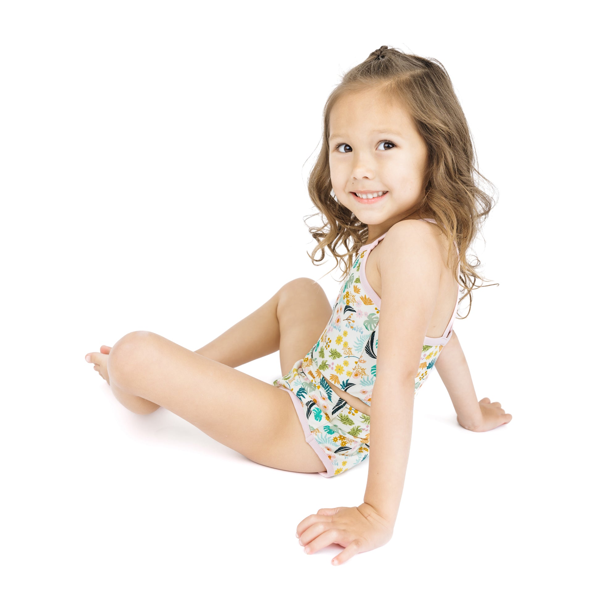 Child sitting while wearing the Tropical Blooms bikini, showcasing the stretchy and lightweight fabric designed for comfort.
