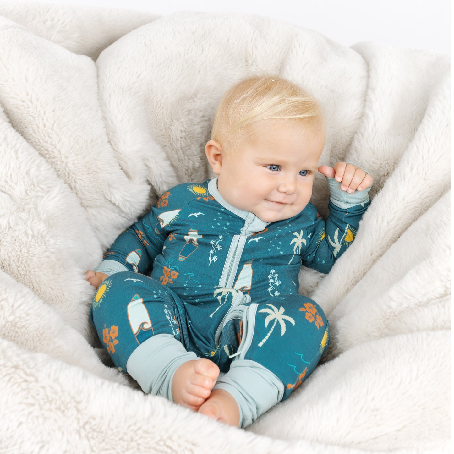 Baby wearing Surf’s Up bamboo pajamas lounging on a soft cushion