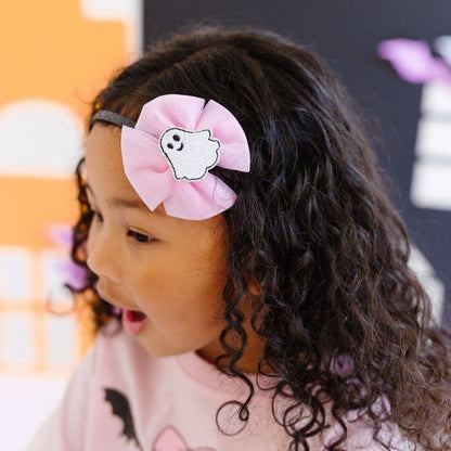 Little girl wearing a Black sparkly headband with a big tulle bow attached and a white ghost in the middle of the bow.