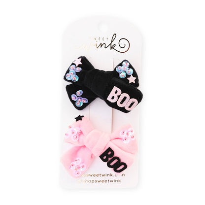 a pack of 2 Halloween themed hair clips. One is velvet black material with sequins stitched onto the ends and the word BOO in pink letters, and the other clip is pink velver with sequins and the word boo in black letters