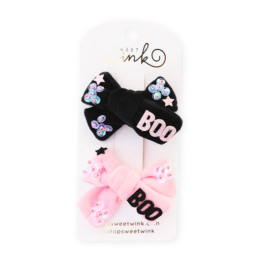 a pack of 2 Halloween themed hair clips. One is velvet black material with sequins stitched onto the ends and the word BOO in pink letters, and the other clip is pink velver with sequins and the word boo in black letters