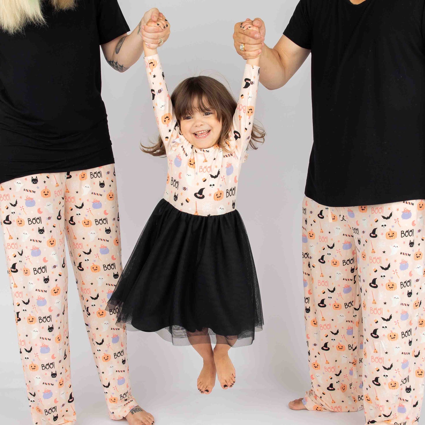 mom and dad swinging little girl in the middle of them on a white backdrop. All 3 people are wearing our Sweet and Spooky pink halloween Print featuring glow in the dark patterns, pumpkins, candy, bats and more!