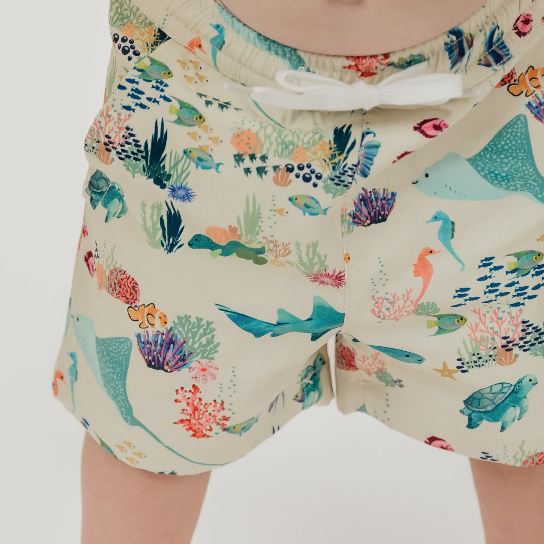 Close up of our Emerson and Friends Coral Reef Boys Swim Trunks, featuring a vibrant ocean-themed design with sharks, sea turtles, and coral, made from quick-dry fabric with UPF sun protection for all-day beach and pool fun.