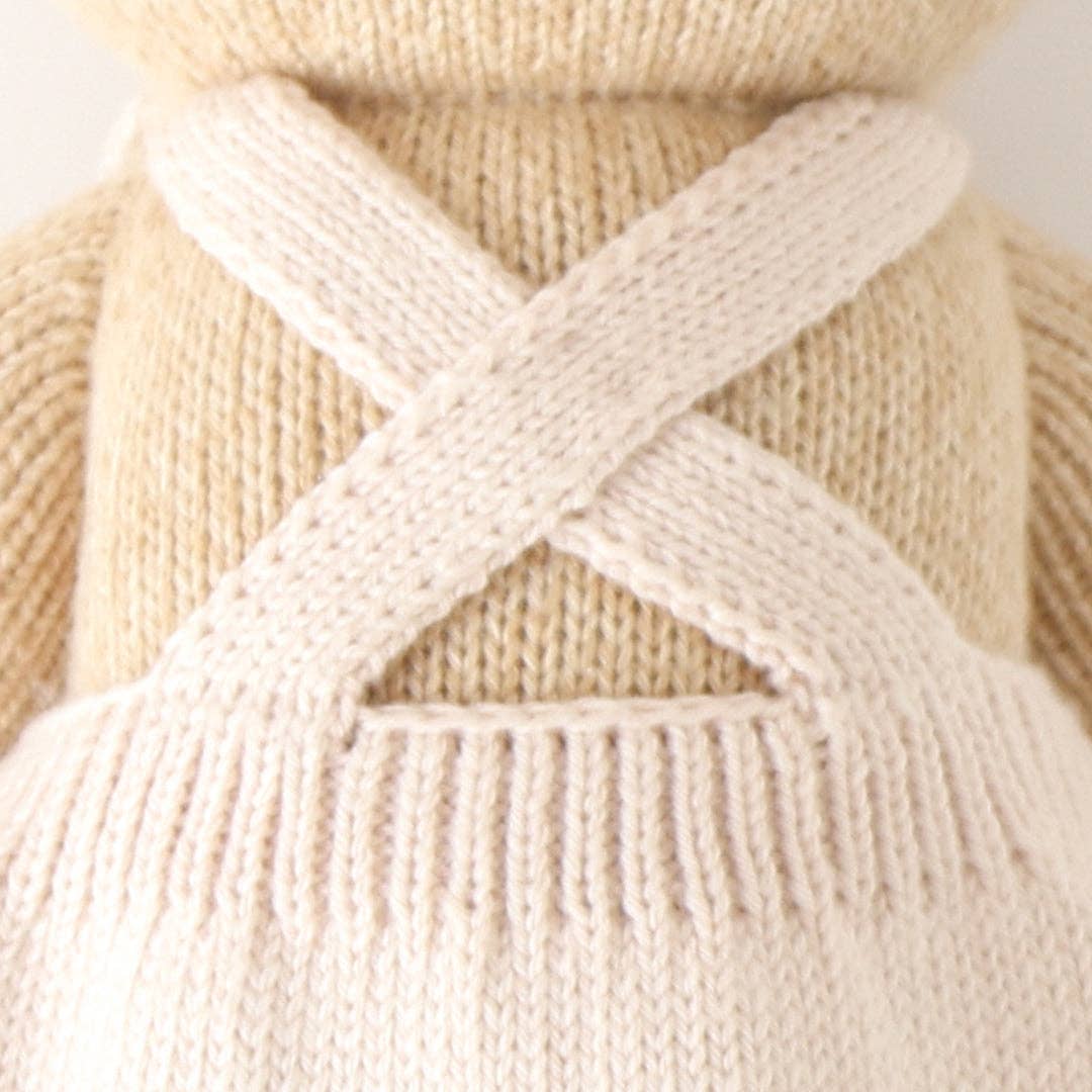 Close-up of a beige knitted sweater with criss-cross pattern on a blurred background