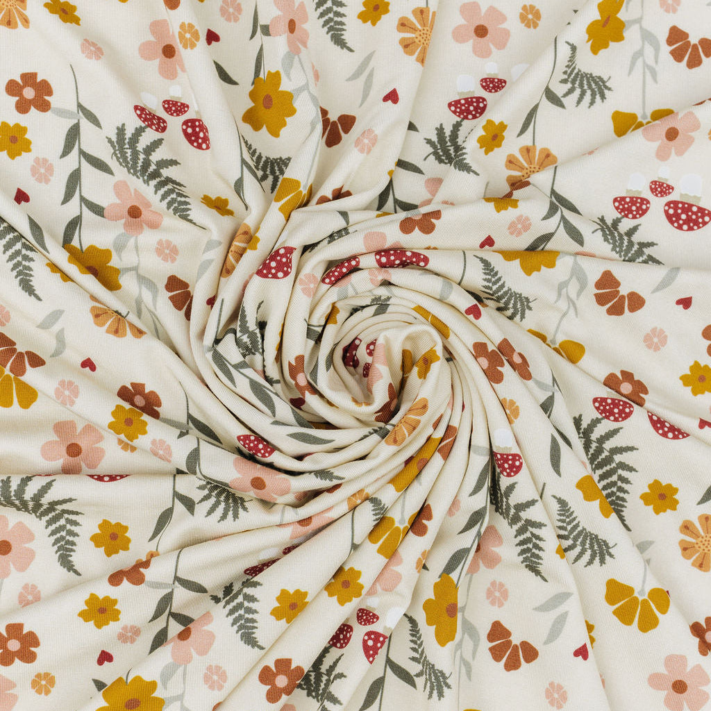 A close-up of a draped fabric with a cream background and a colorful floral pattern featuring yellow, orange, pink, and green flowers and leaves, arranged in a spiral drape.