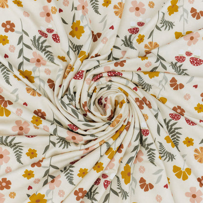 A close-up of a draped fabric with a cream background and a colorful floral pattern featuring yellow, orange, pink, and green flowers and leaves, arranged in a spiral drape.