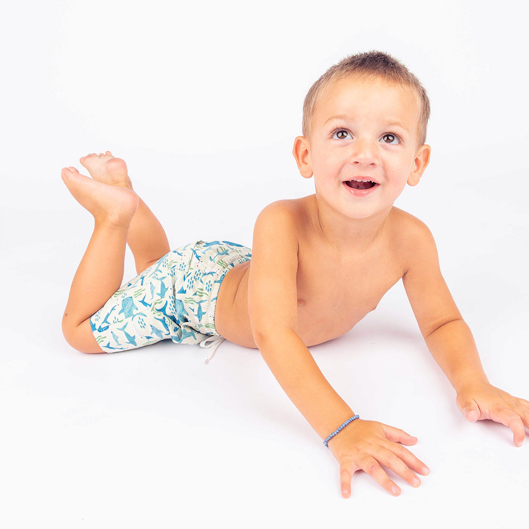 Little boy laying down wearing the Shark Friends Boys Swim Trunks.