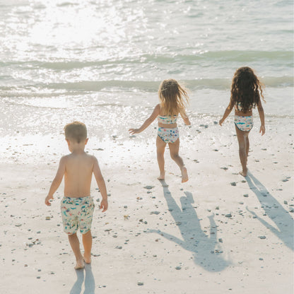Toddler friends walking into the beach in a Coral Reef Bikini Swimsuit featuring a vibrant two-piece ocean print with sharks and sea turtles, made from breathable, UPF 50+ fabric for sunny beach adventures.