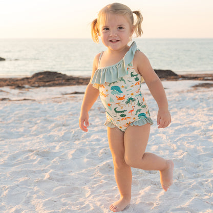 A toddler girl walking on the sand in the Explore Florida one-piece swimsuit, highlighting the comfortable movement for beach play.