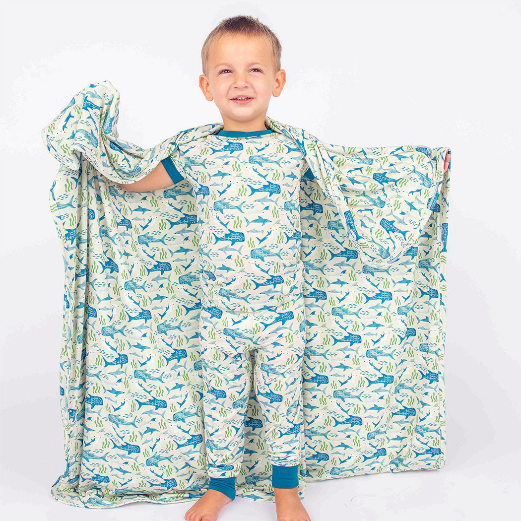 Little boy wearing our Shark Friends Two Piece Bamboo Pajama Set, holding up our Shark Friends Bamboo Blanket.