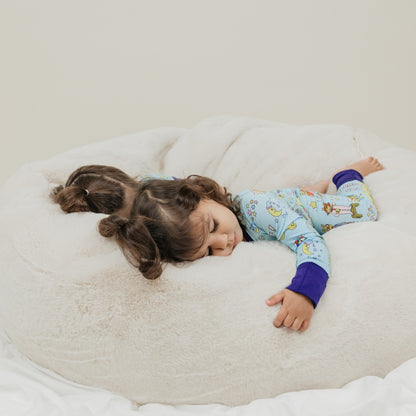 A baby girl sleeping in with our convertible pajama from our PBS Good Night Arthur™ collaboration, featuring a cozy bedtime scene with Arthur and friends, storybooks, toothbrushes, bunny slippers, a sleeping puppy, crescent moons with sleep caps, twinkling stars, and the words "GOOD NIGHT!" on a soft blue background.