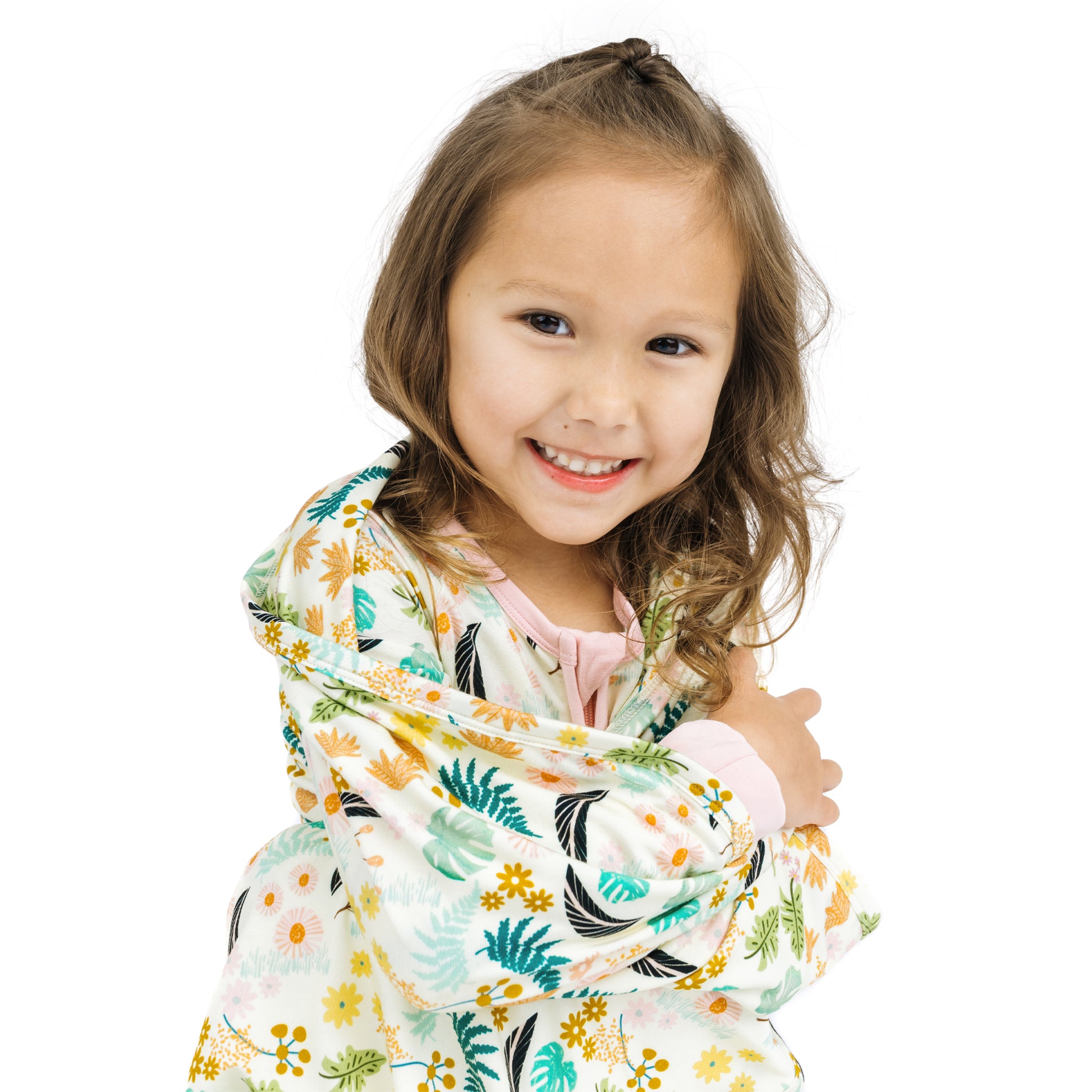 A smiling toddler girl wrapped in the soft Tropical Blooms bamboo blanket, showing the comfortable and cozy material.