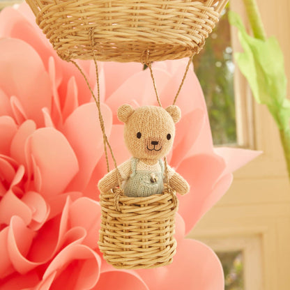 Knitted teddy bear in a wicker basket against a pink floral background