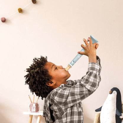little boy blowing into a light blue wooden toy trumpet