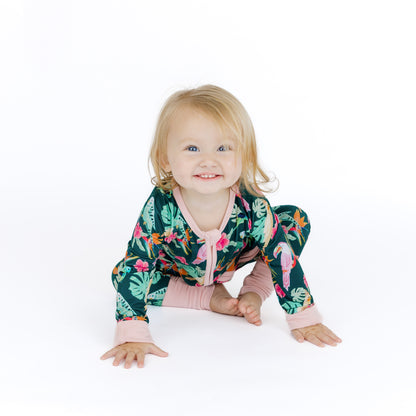 Baby sitting comfortably in the Isla Botánica tropical birds print sleeper, showcasing the breathable and moisture-wicking bamboo.