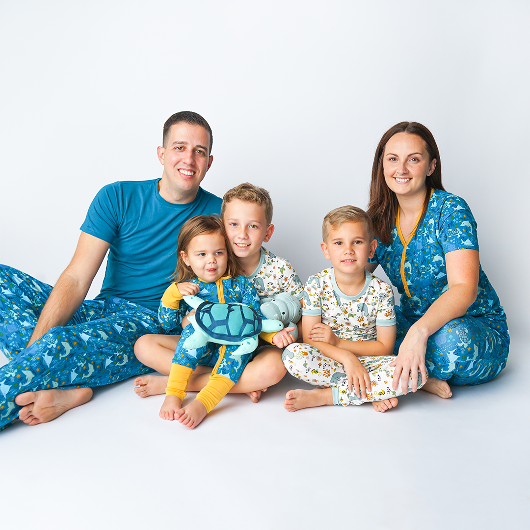 family sits on the floor in the "ocean friends" and "manatee" pajamas. one child sits and holds Toby the turtle and the other one hold Max the Manatee.