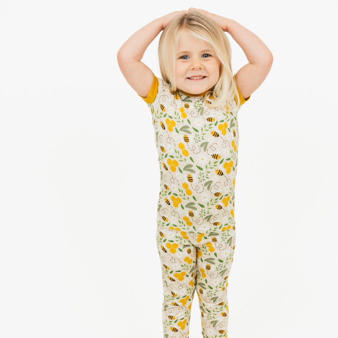 Smiling child wearing a two-piece bamboo pajama set featuring a happy honey bee and floral print. Soft, breathable, and hypoallergenic for a cozy and comfortable sleep.