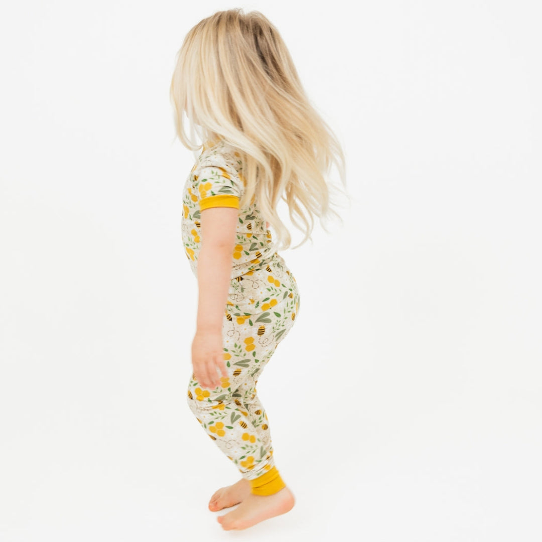 A toddler girl in breathable, hypoallergenic bamboo pajamas with a cute honey bee and flower print, walking with her long blonde hair flowing.