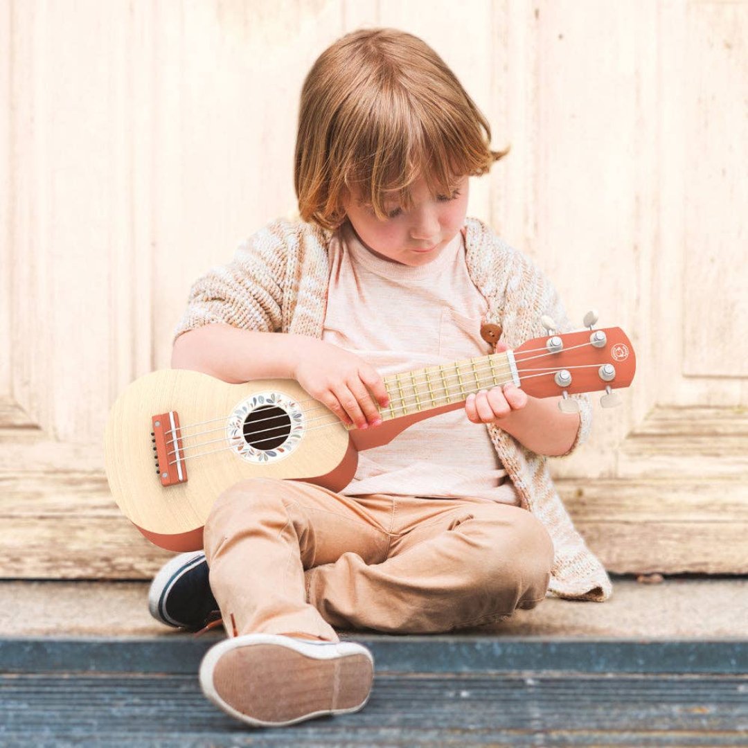 little boy playing kids sized toy ukulele