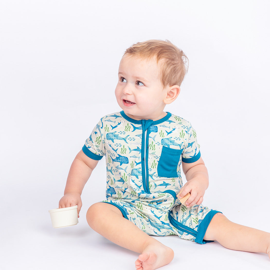 Little boy sitting while wearing our Shark Friends Shortie Romper.