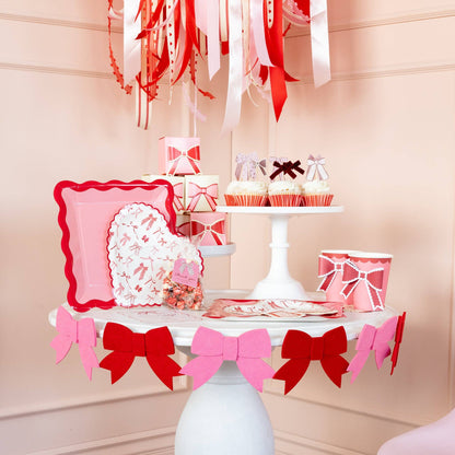 Decorative table setting with pink and red bows, plates, and cups on a white surface.