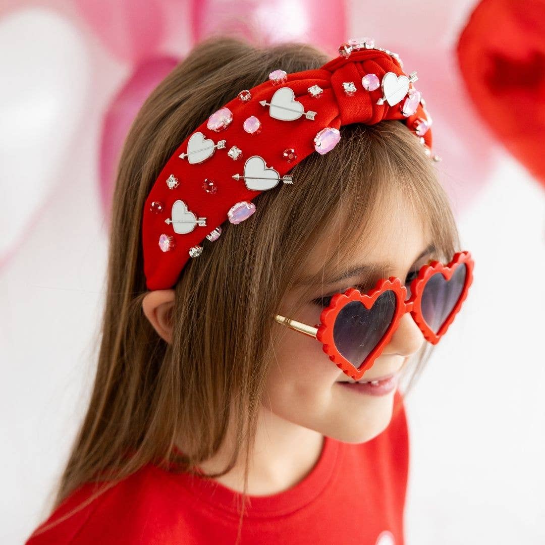 little girl wearing a red headband with valentines themed gemstones on it