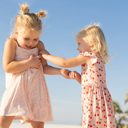 Two young girls in matching dresses standing outdoors against a clear blue sky.