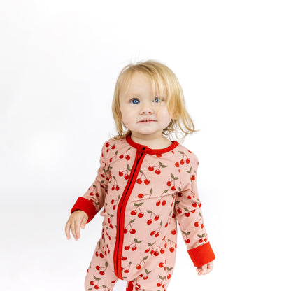 Child wearing a pink onesie with cherry pattern on a white background
