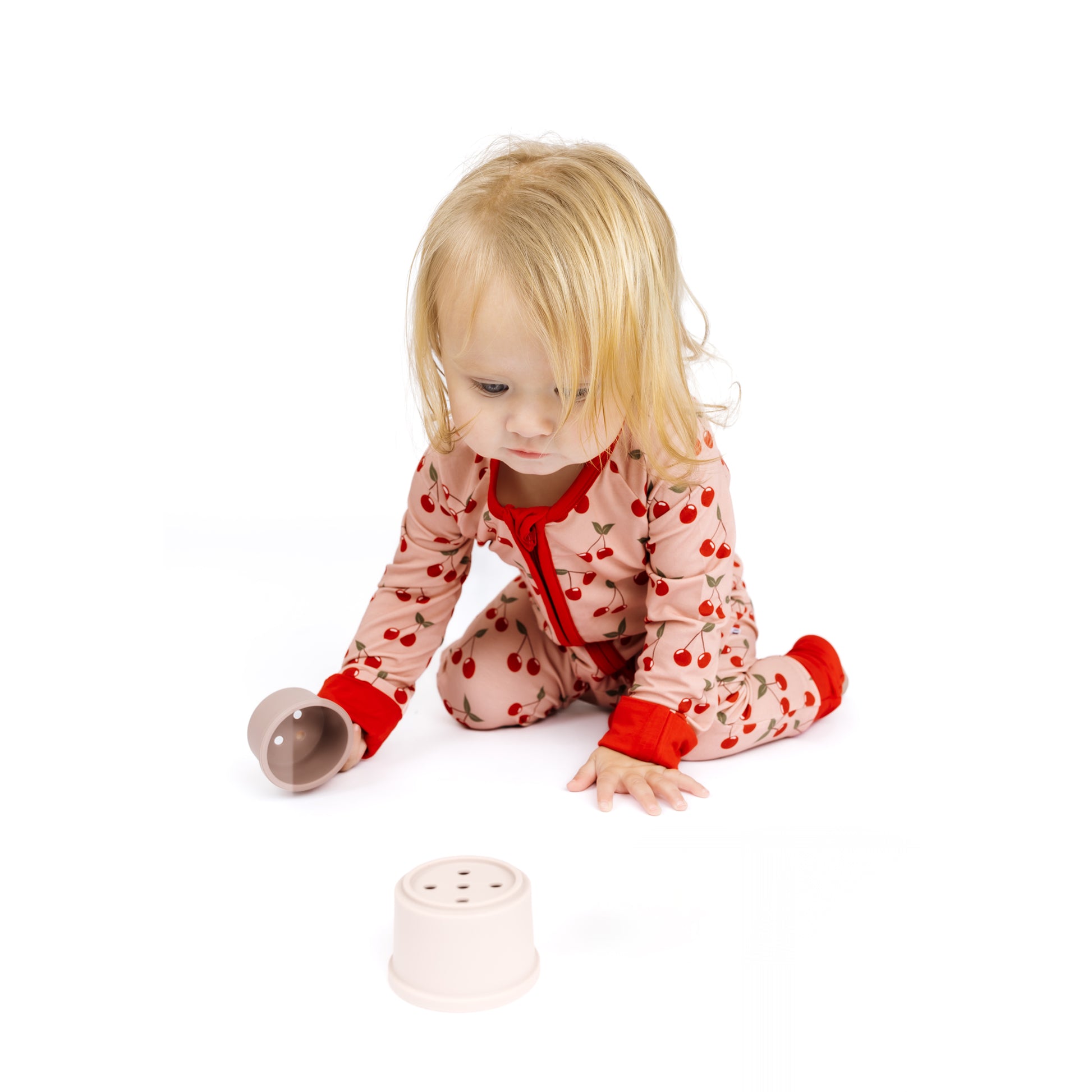 Child in a pink onesie with red accents playing with a toy on a white background