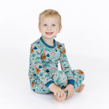 Child sitting in volcano dinosaurs bamboo two-piece pajama set.