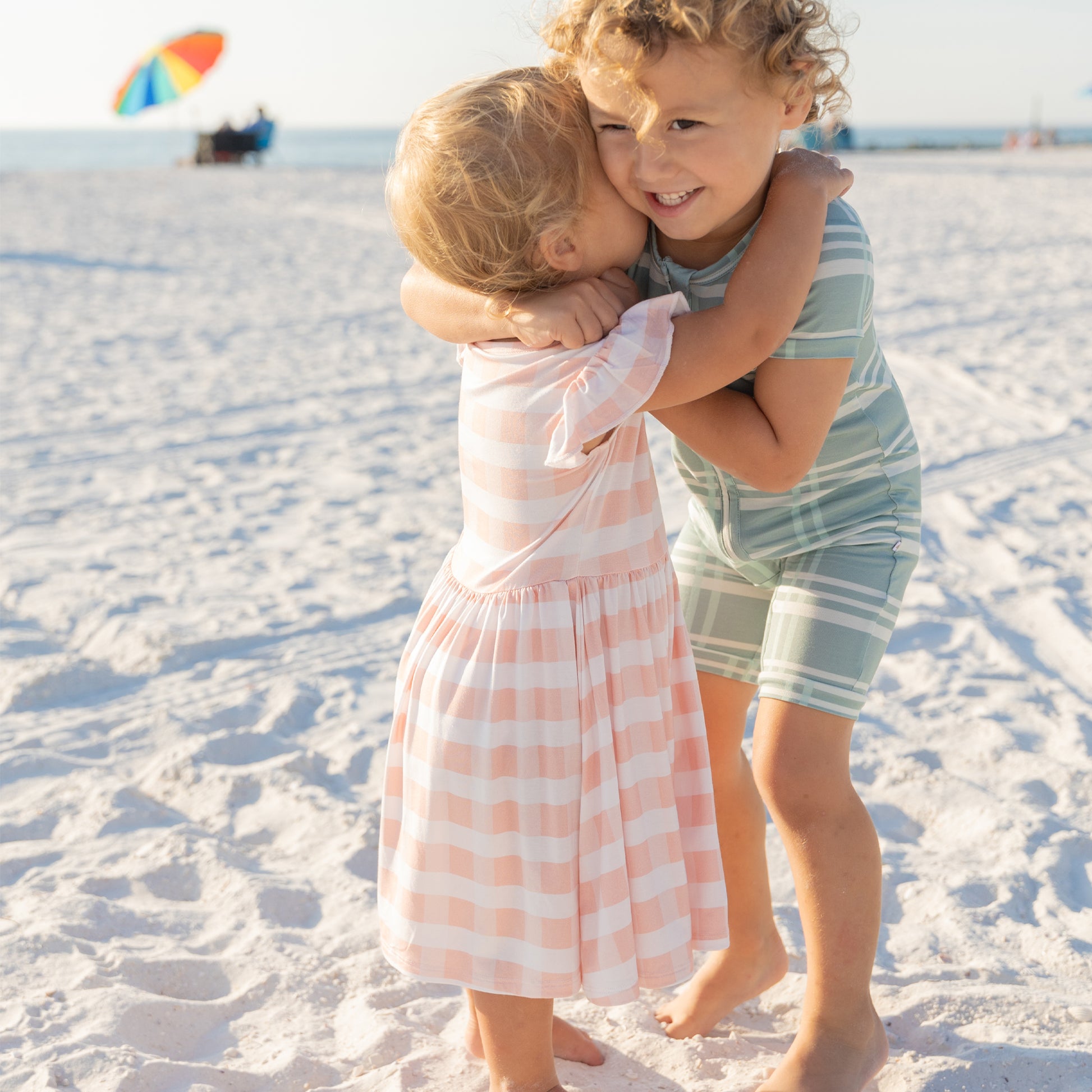 Two children hugging on the beach, highlighting the soft and comfortable fabric of the pink gingham twirl dress.