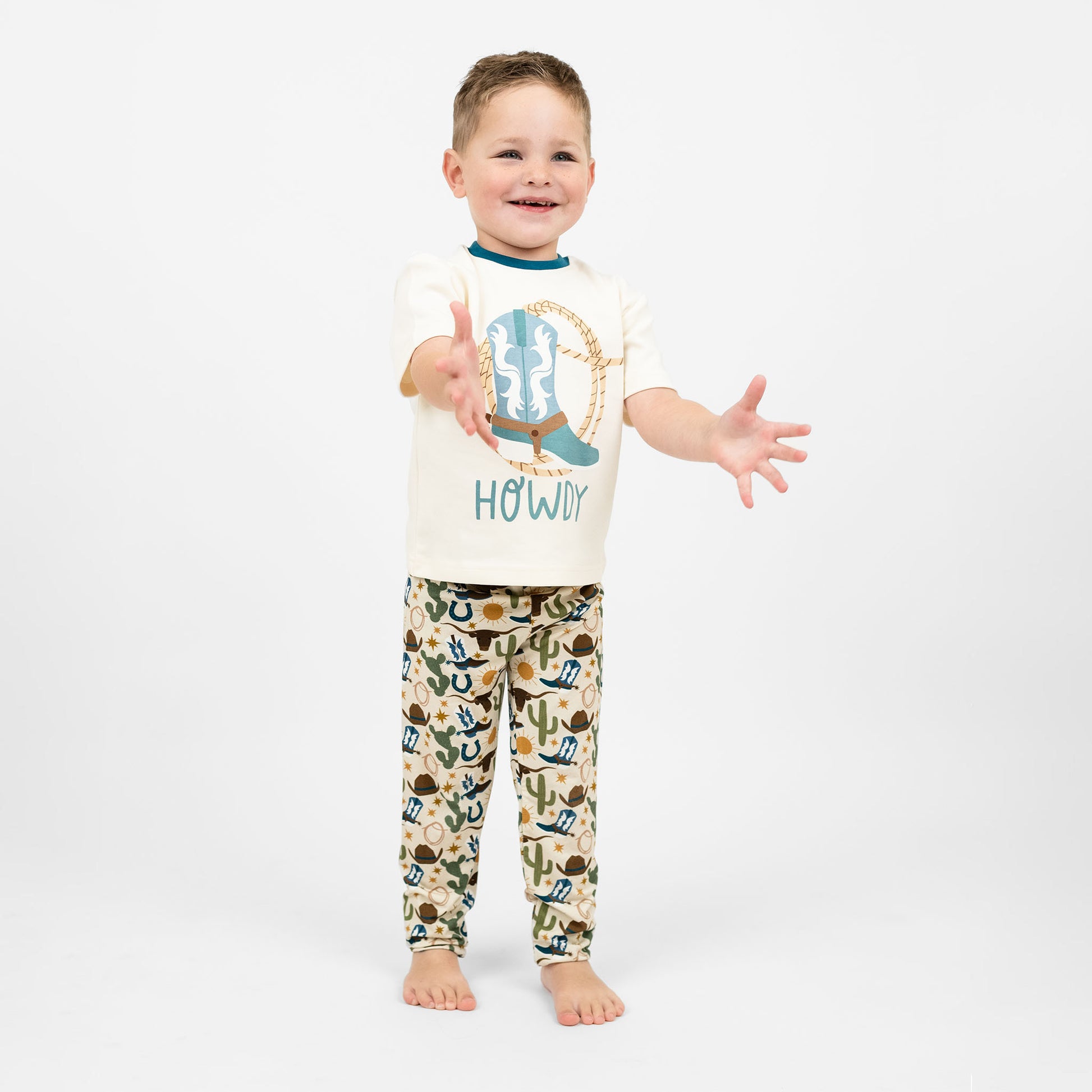 A toddler boy wearing our Howdy Cotton shirt featuring the word "Howdy" in playful, blue letters, perfect for a western outfit.
