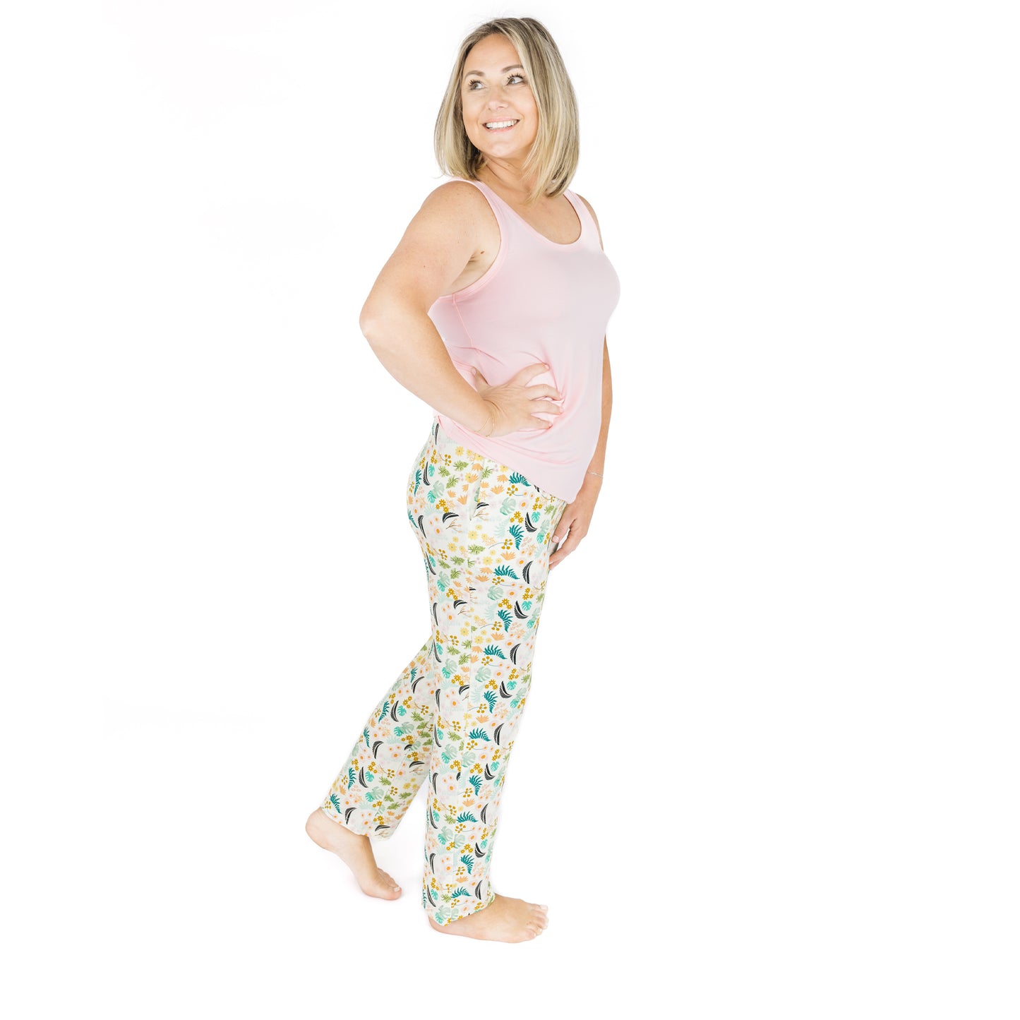 A woman standing in Tropical Blooms bamboo lounge pants paired with a pink tank top, showing the flattering unisex fit.