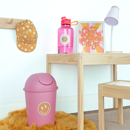 the yellow happy face sticker is placed on a trash can next to a cute desk. 