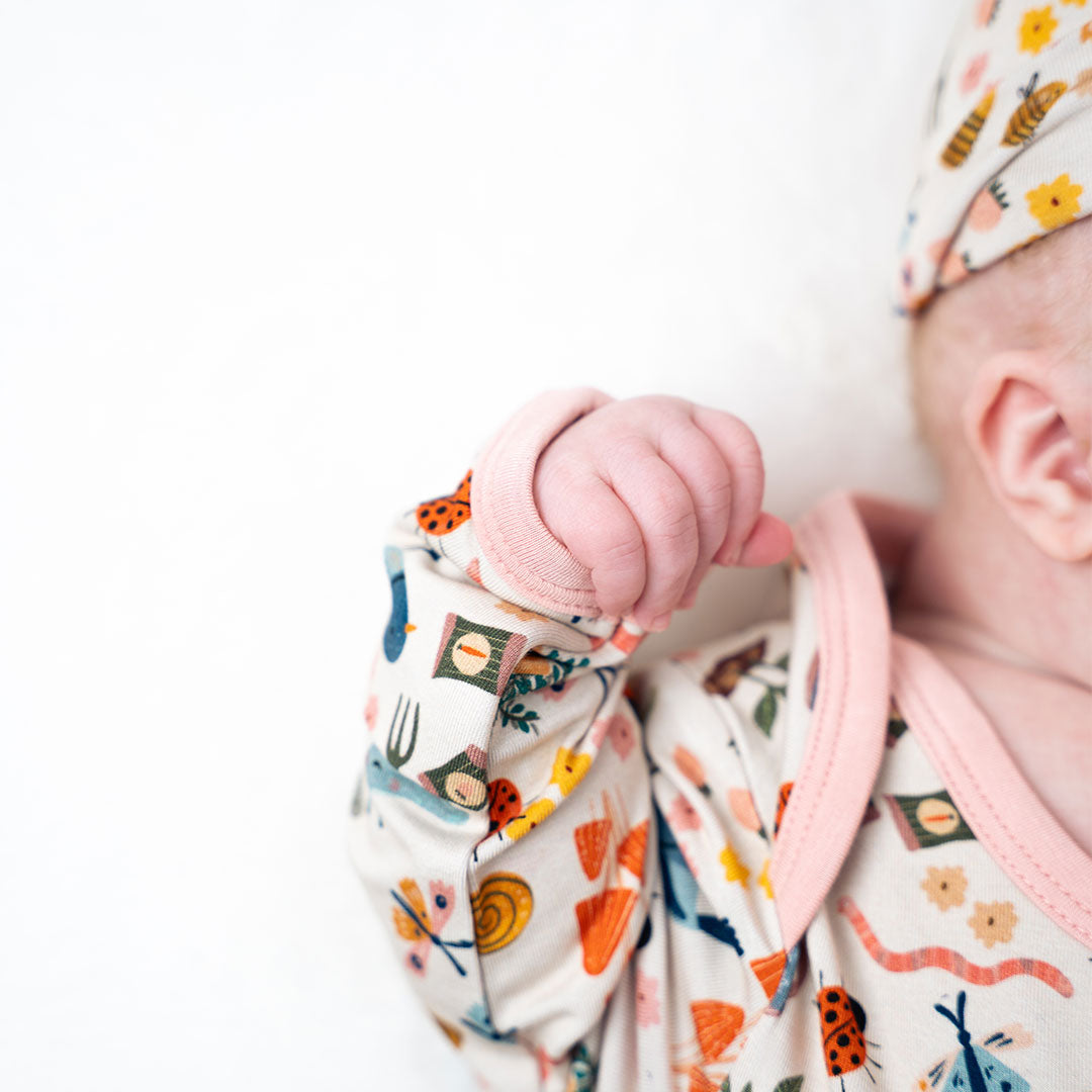 Baby showcasing our convertible Garden Friends pajama on a white background. The print showcase ladybugs, butterflies, flowers, birds, snails, cactus, bees and plants. 
