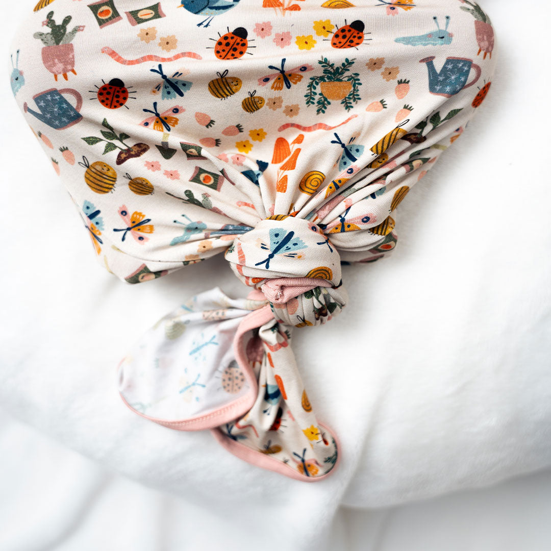 Baby showcasing our convertible Garden Friends pajama on a white background. The print showcase ladybugs, butterflies, flowers, birds, snails, cactus, bees and plants. 