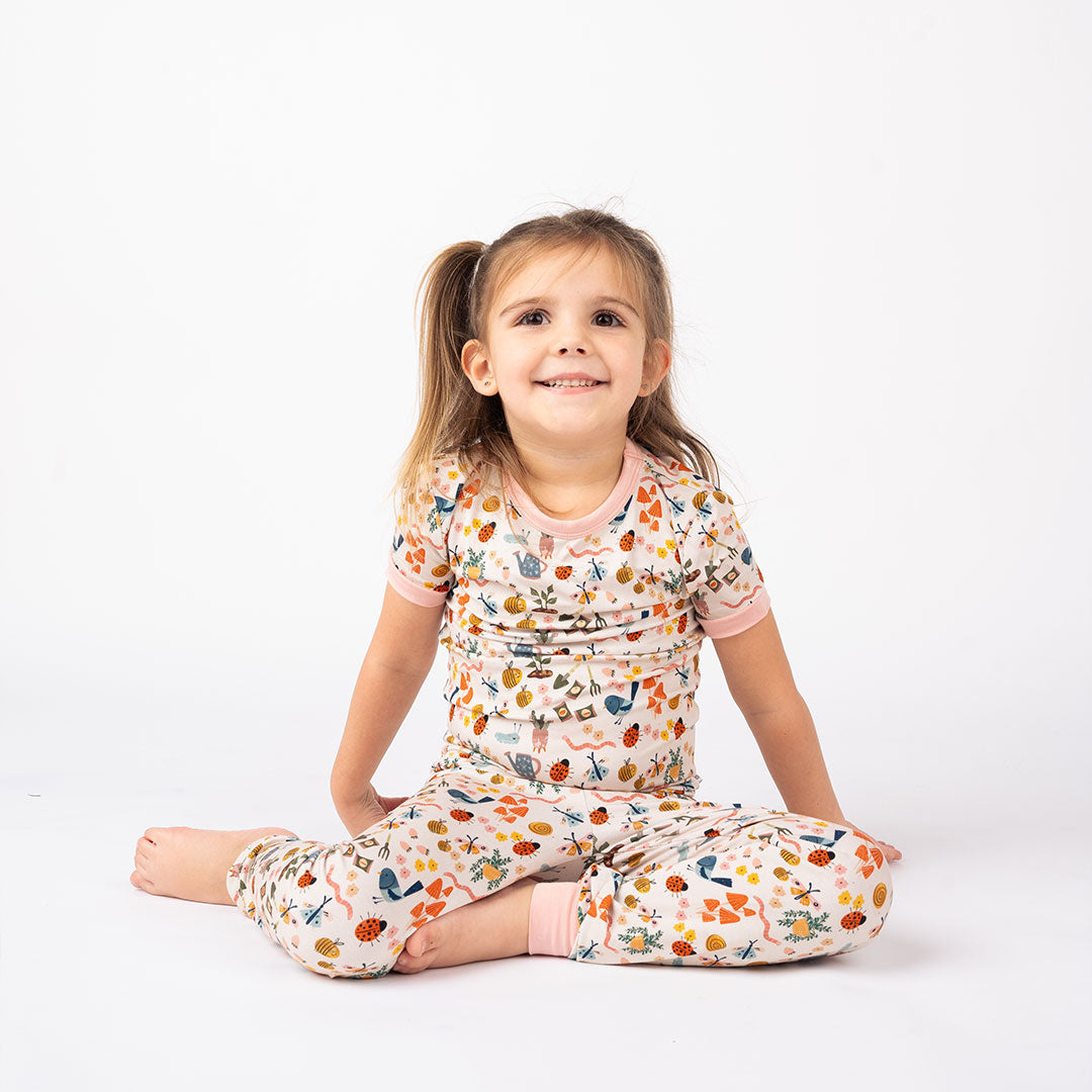 Toddler showcasing our Garden and Friends 2 Set Pajama on a white Background. The print showcase ladybugs, butterflies, flowers, birds, snails, cactus, bees and plants. 